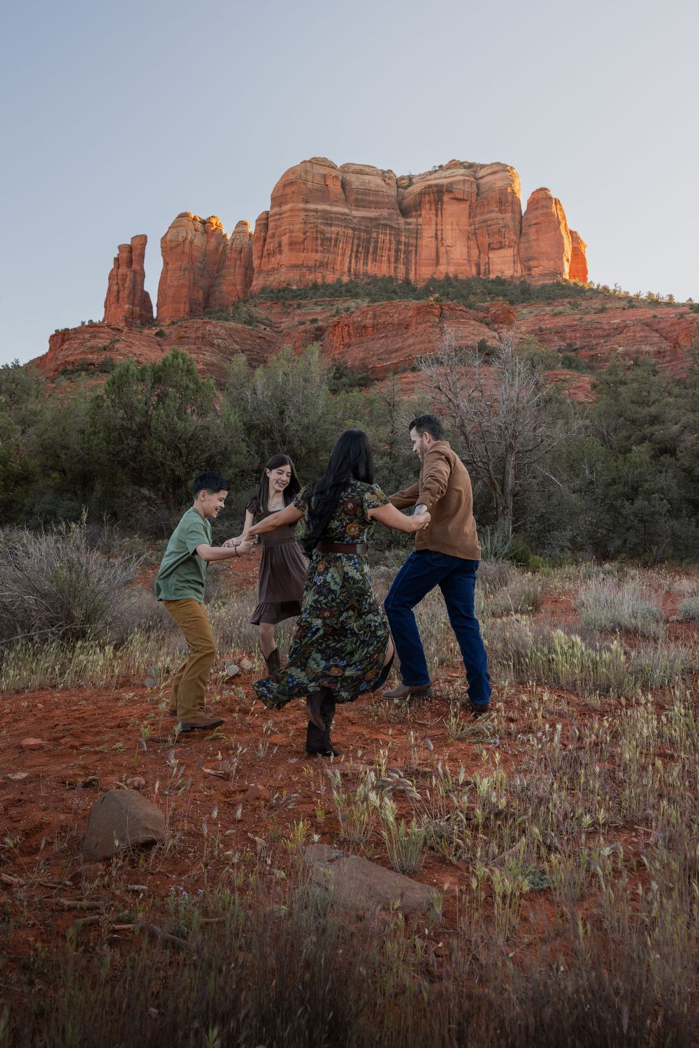 Group of four friends dancing joyfully in front of Cathedral Rock in Sedona at sunset.