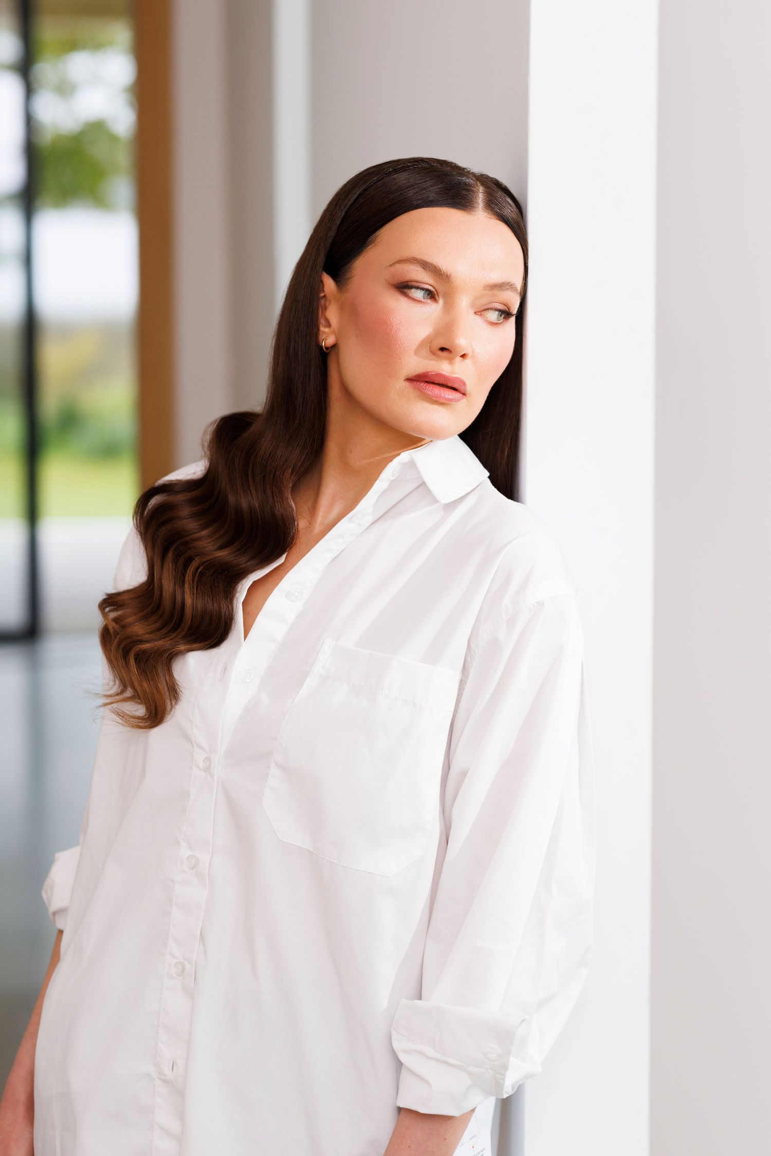 Professional style portrait in white button-down shirt against bright window background.