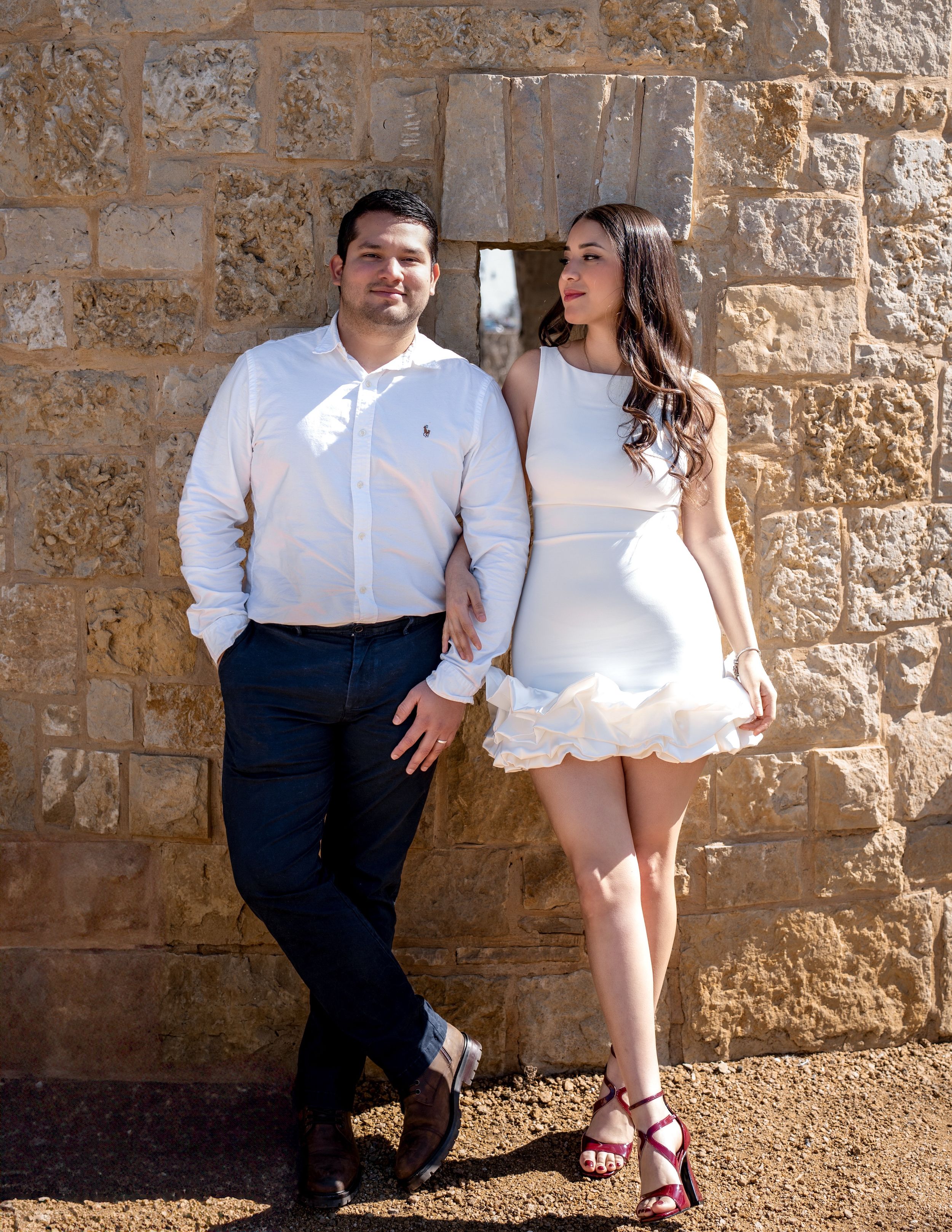 Engagement photo of a couple in casual elegance against rustic stone walls — captured in Grapevine, Texas.