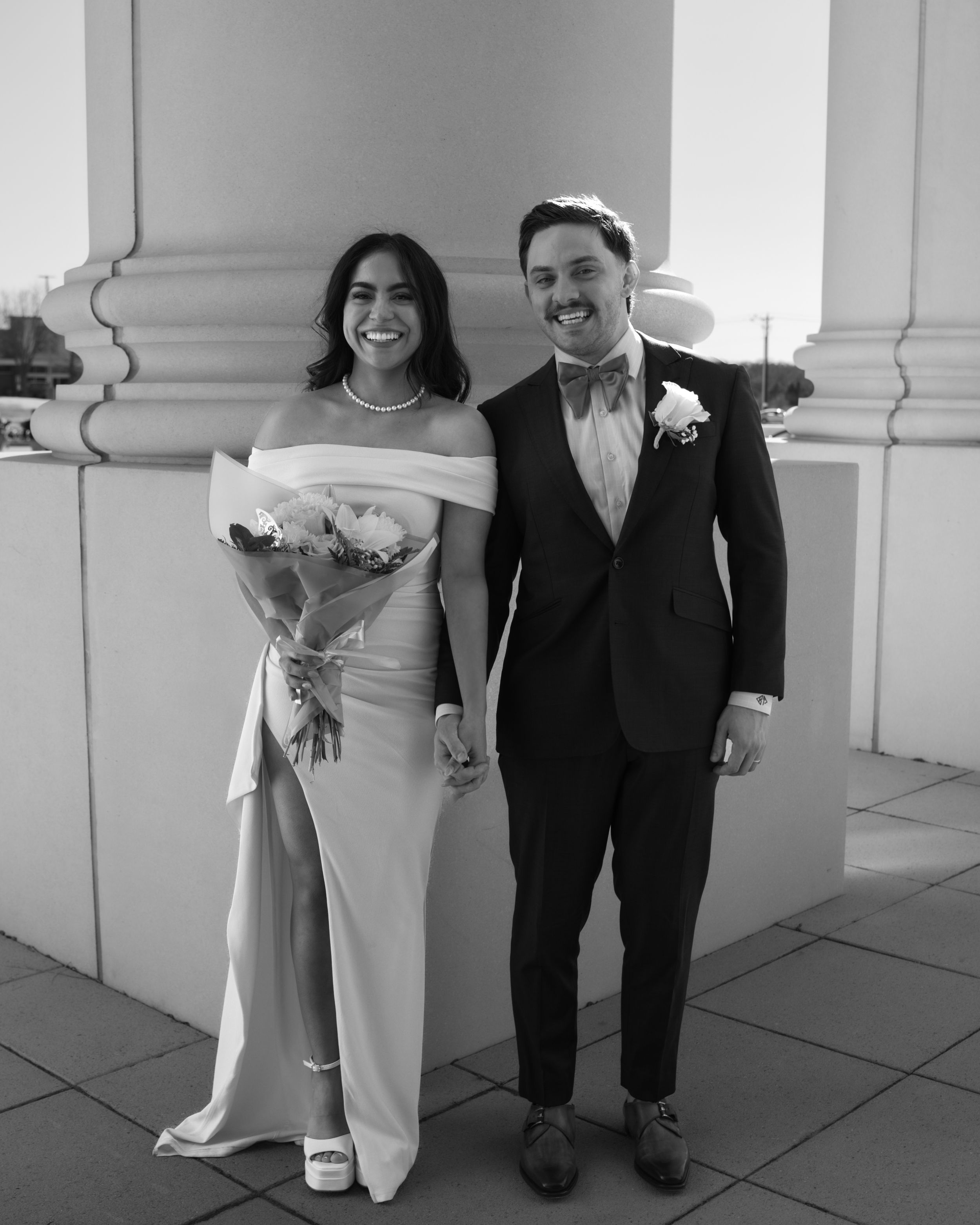 Joyful bride and groom standing together in elegant wedding attire, captured in a classic black and white portrait.