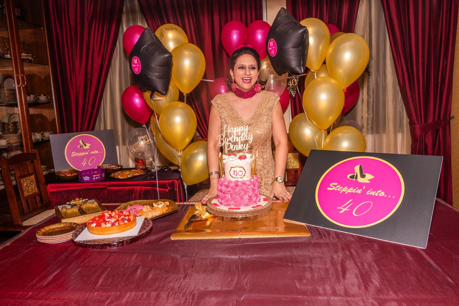 Birthday celebration setup with gold and pink balloons around decorative table.