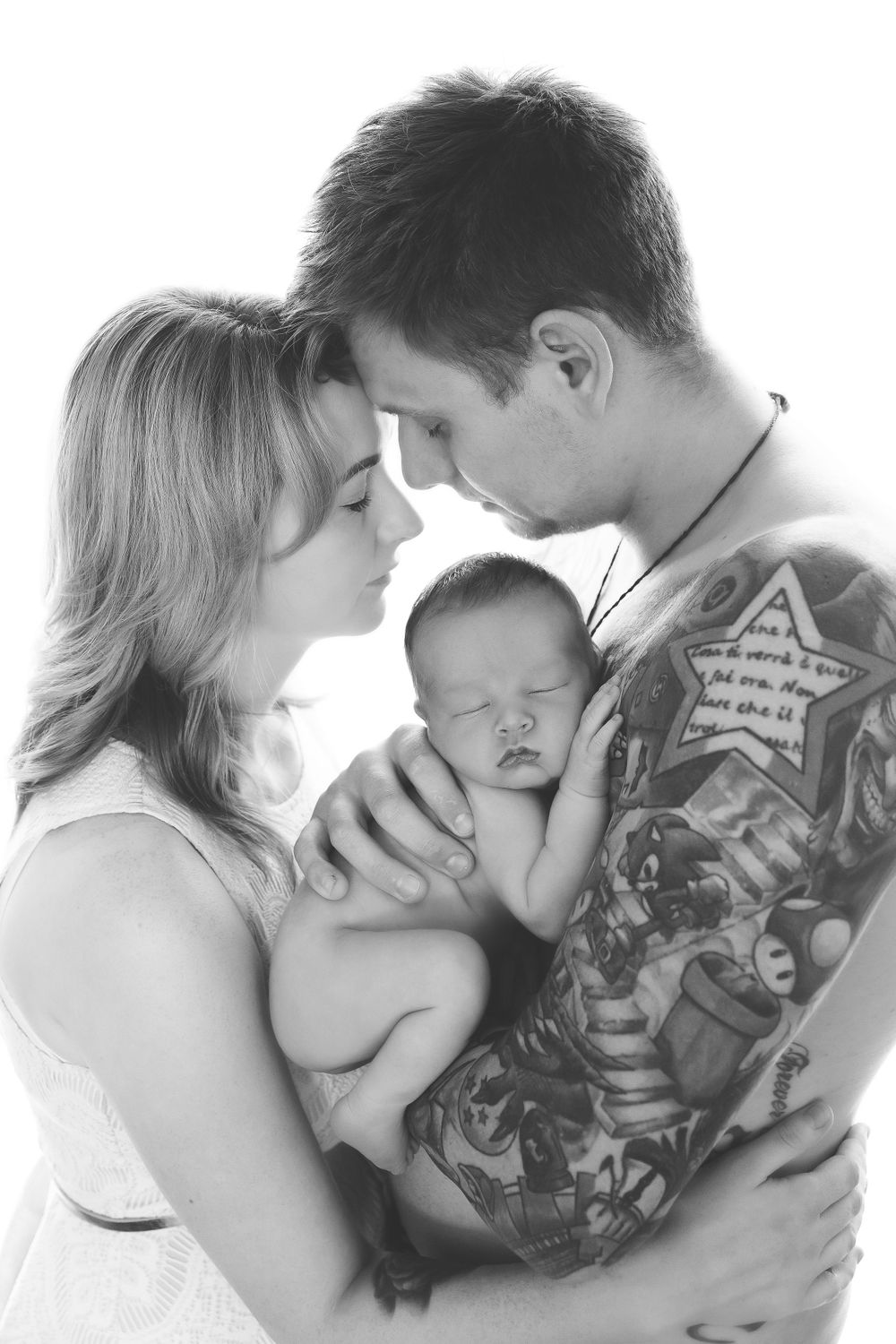 Black and white intimate portrait of parents sharing tender moment with sleeping newborn.