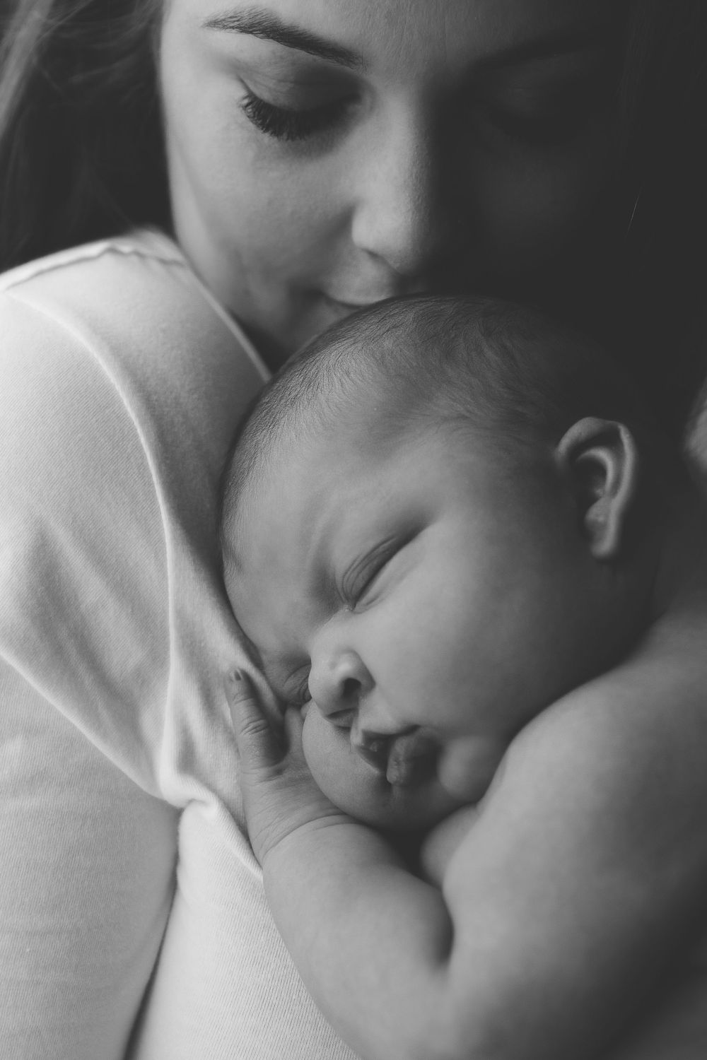 Black and white portrait of peaceful sleeping newborn being held against white sweater.