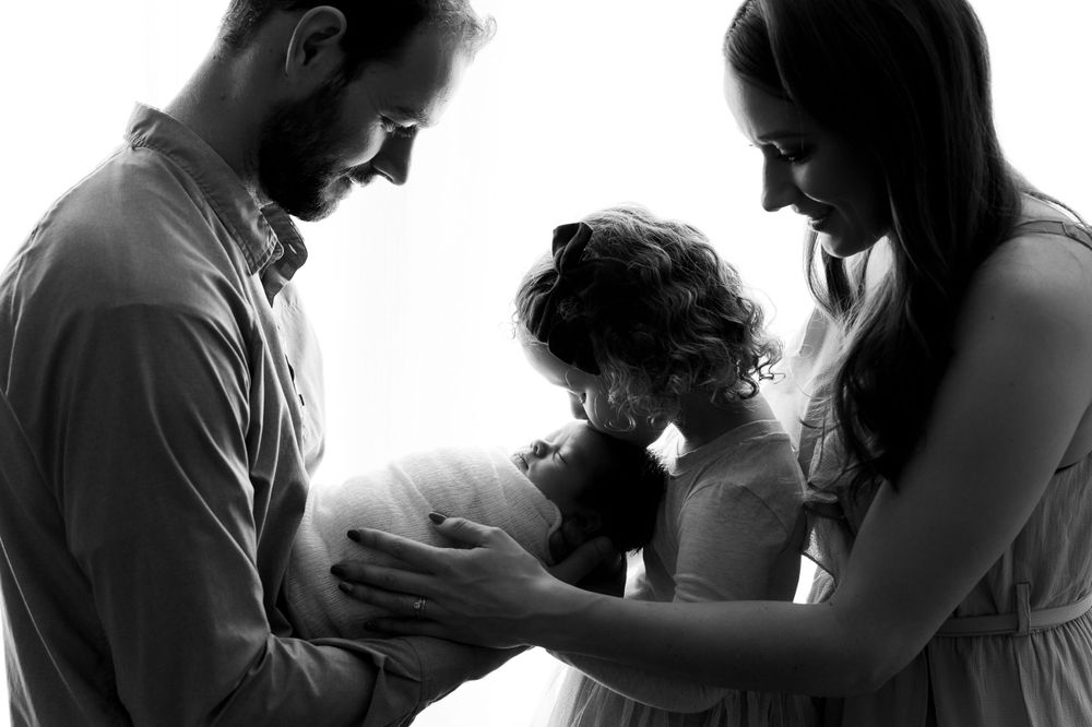 Black and white silhouette of family sharing intimate moment with newborn baby.