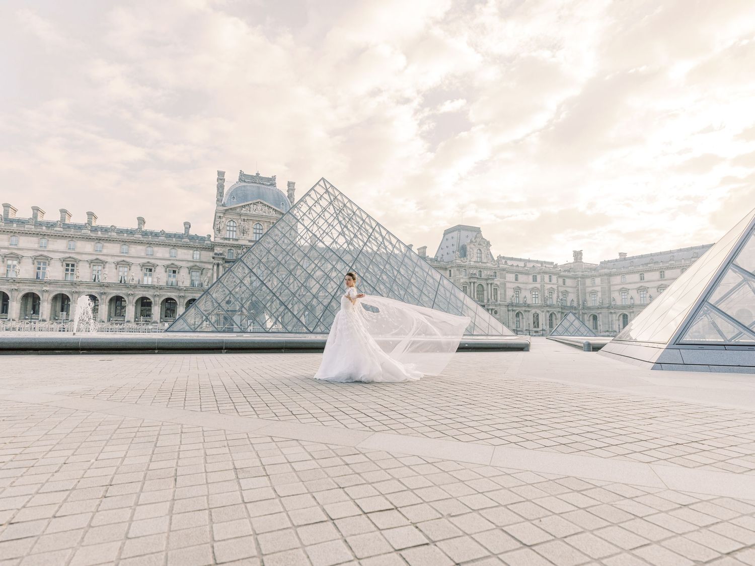 Glass pyramid entrance to the Louvre Museum in Paris stands against historic palace architecture at dusk.