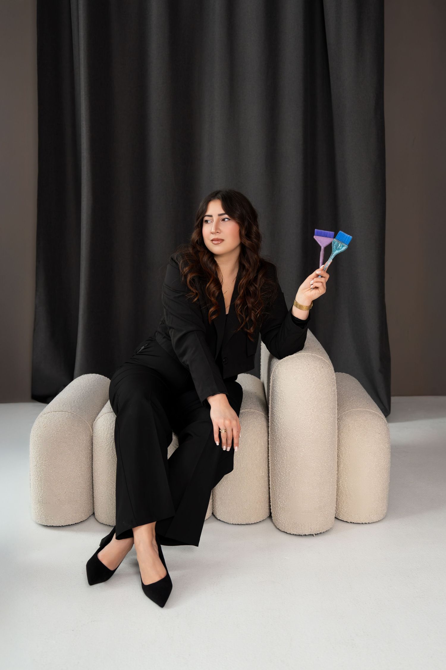 Elegant woman in black pantsuit sitting on modern couch holding colorful party accessories.