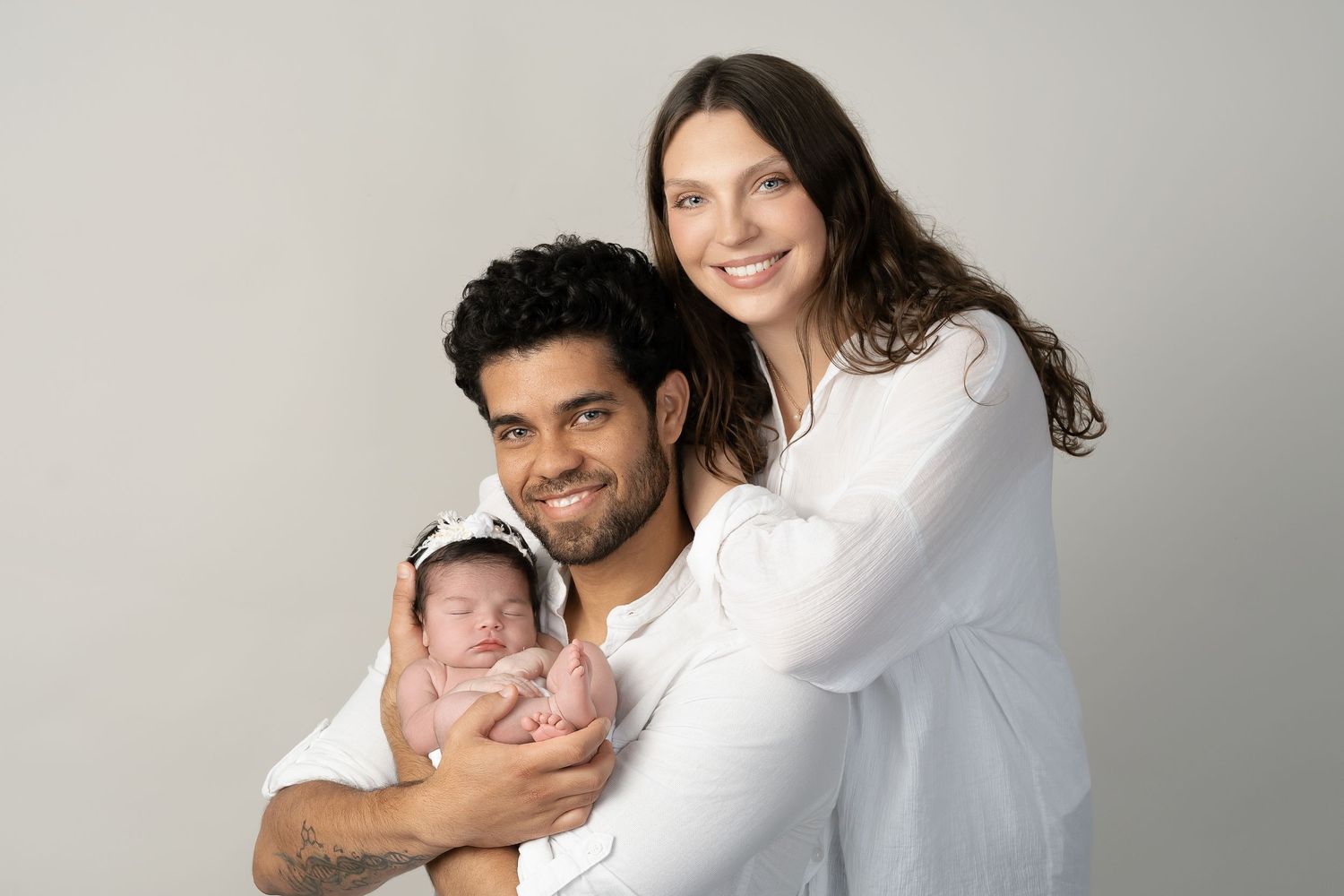Family wearing white poses together for a studio portrait against a light gray background.