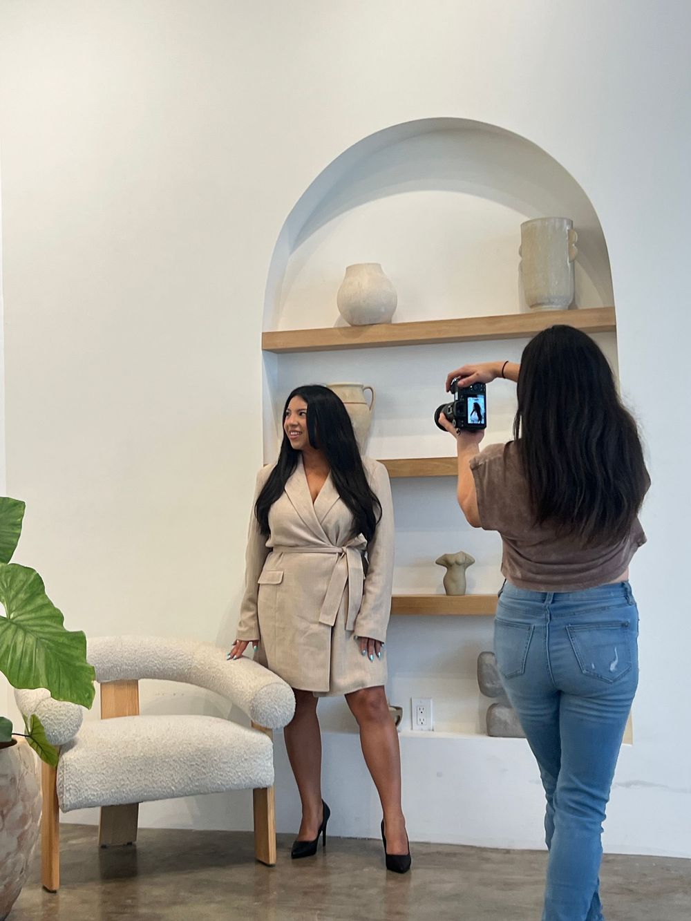 A woman in a beige wrap dress poses for a photo in a modern white interior studio space.