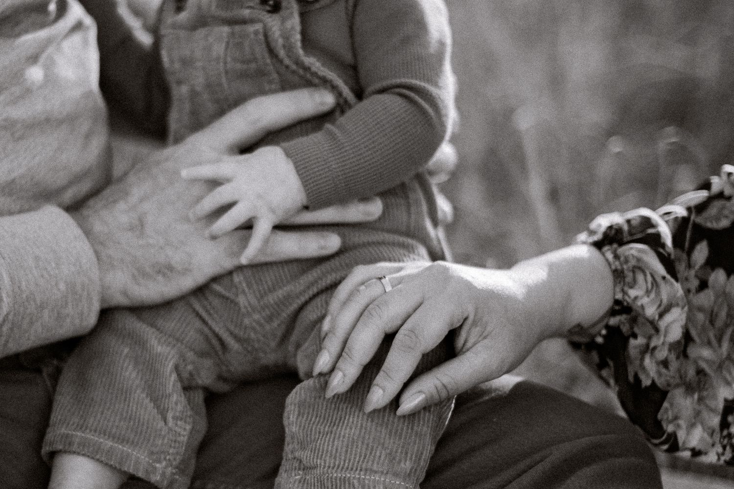 Black and white closeup photograph showing hands resting gently on denim-clad legs.