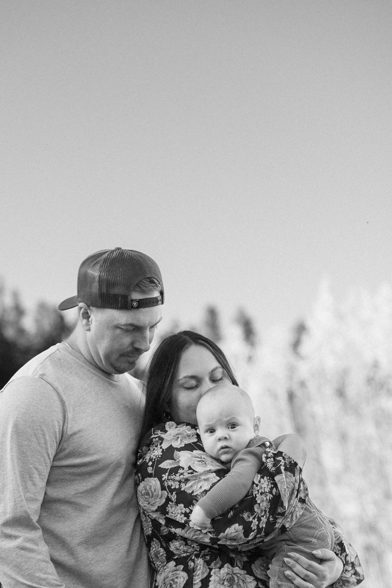 An intimate black and white family portrait showing a tender moment outdoors against a soft background.