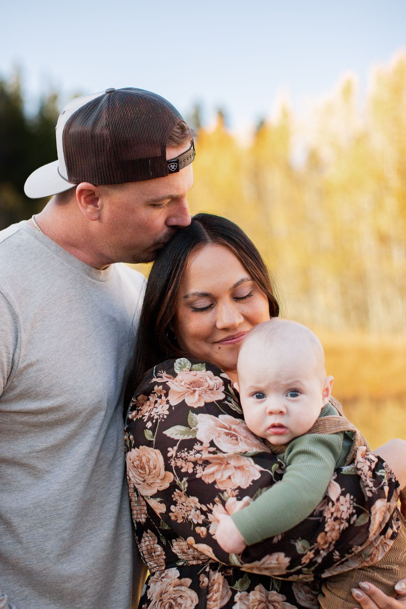 A tender outdoor family moment captured during golden hour amongst autumn grass with warm sunlight in the background.