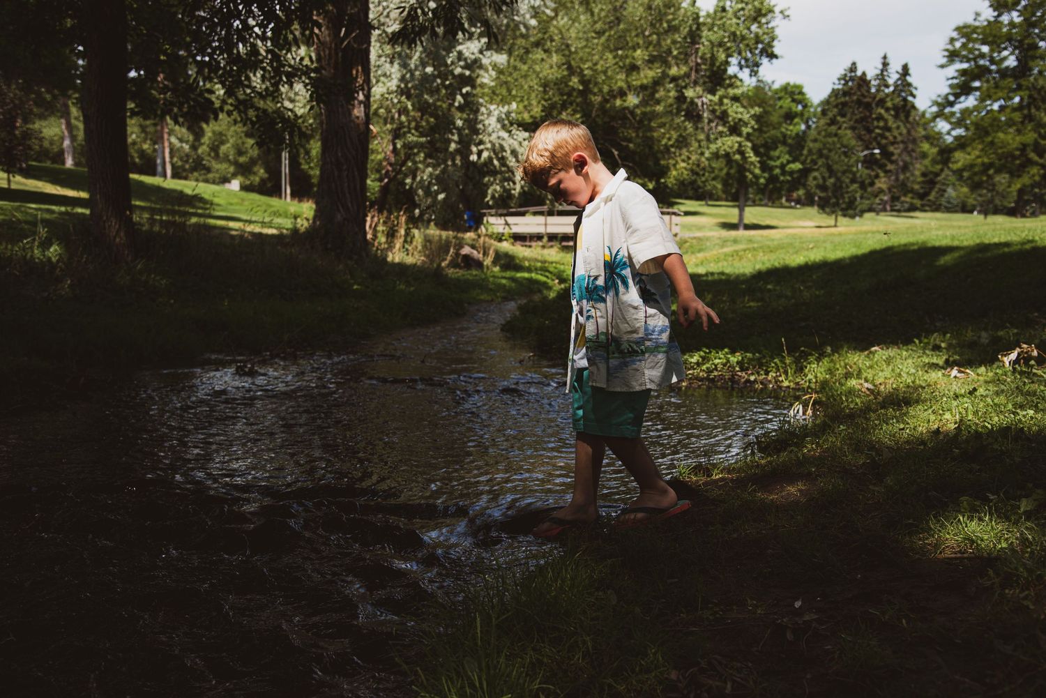 Young boy walking barefoot through a muddy stream in a shaded park