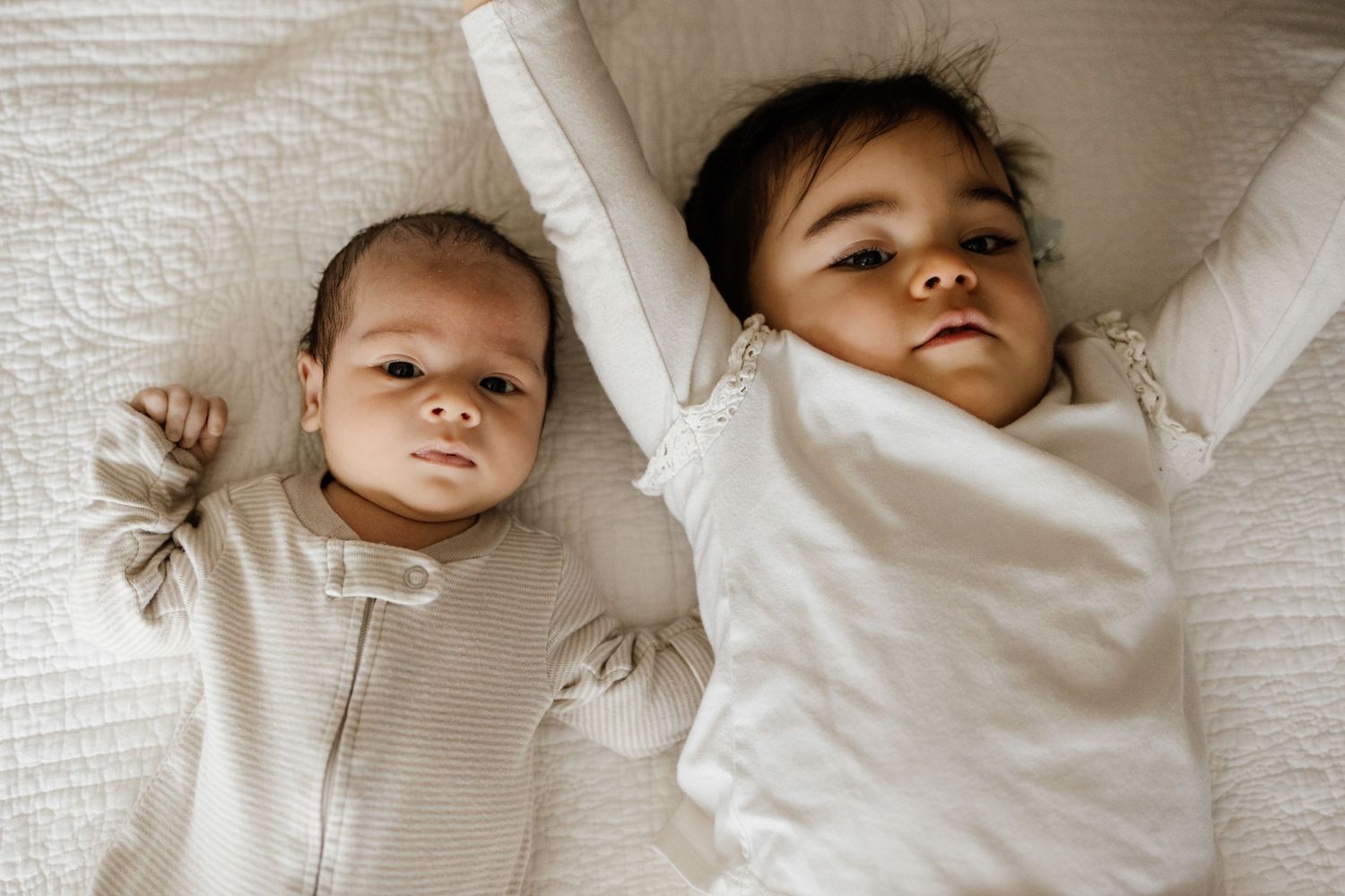 Siblings lay next to each other on a bed at a newborn photoshoot in San Jose