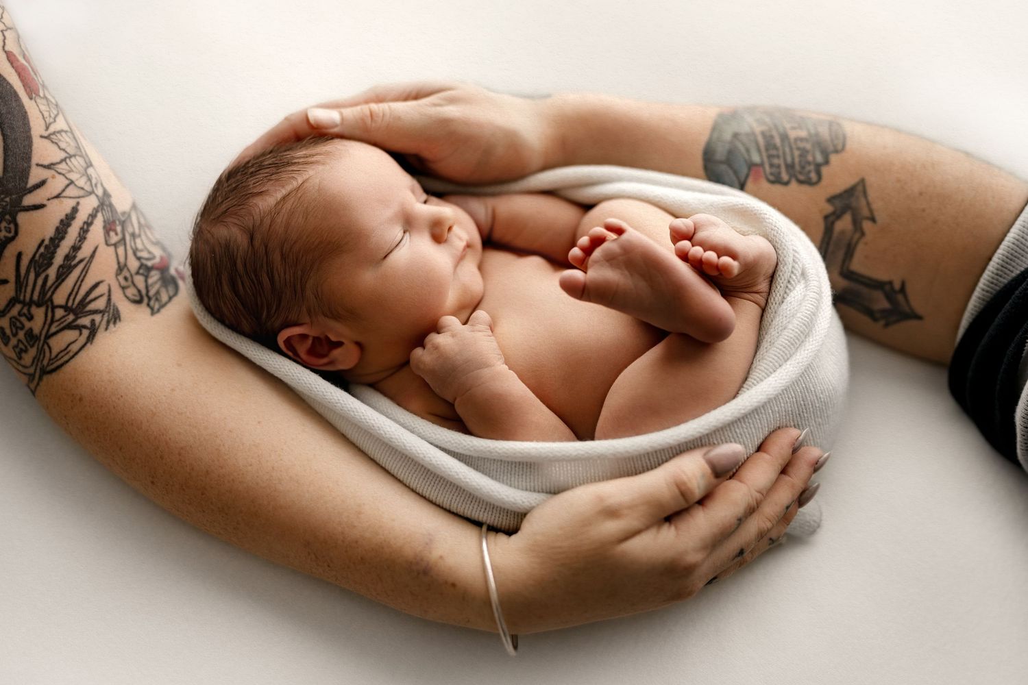 Peaceful newborn baby wrapped in soft white blanket during portrait session against neutral background.