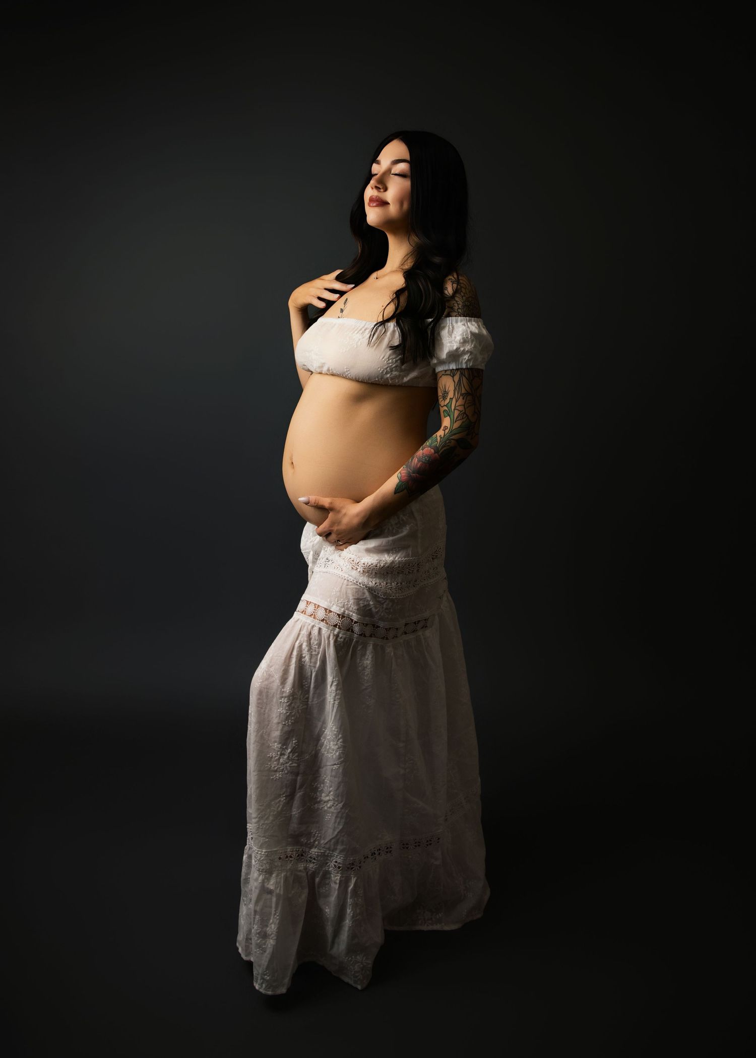 Salt Lake City Maternity Photographer Expectant mother wearing white lace dress - dramatic studio lighting with dark background.