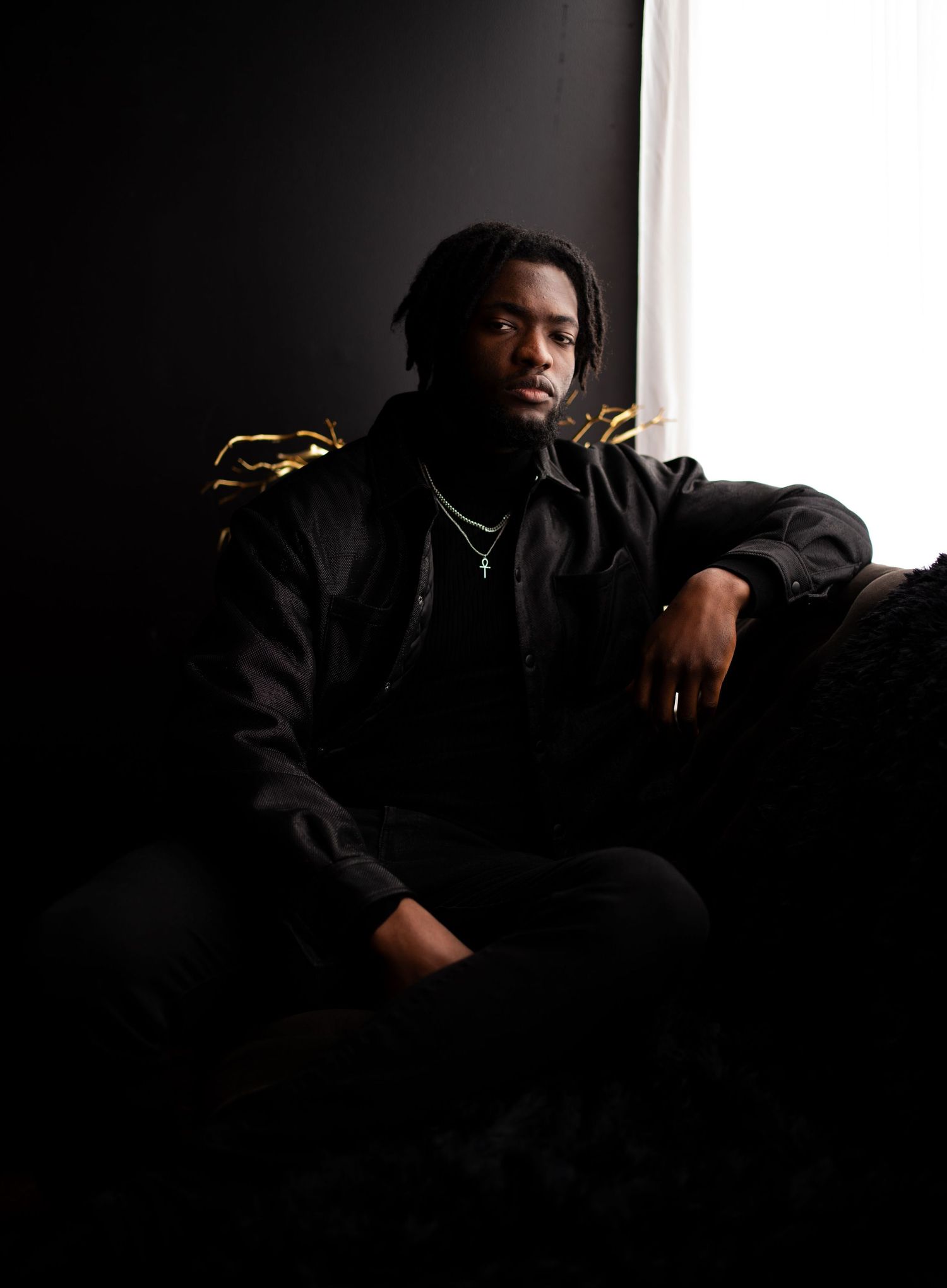 Artistic portrait of someone in black clothing against a dark background with dramatic side lighting.