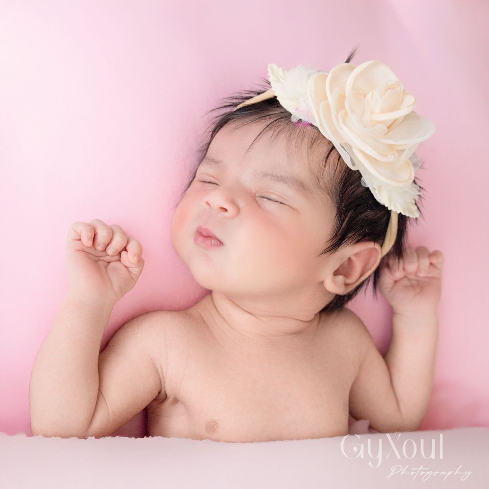 Sleeping newborn with cream floral headpiece against soft pink background.