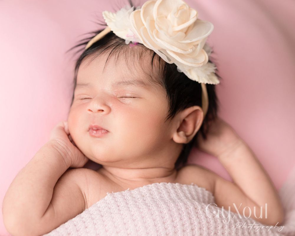 Peaceful sleeping newborn wearing white rose crown against pink backdrop.
