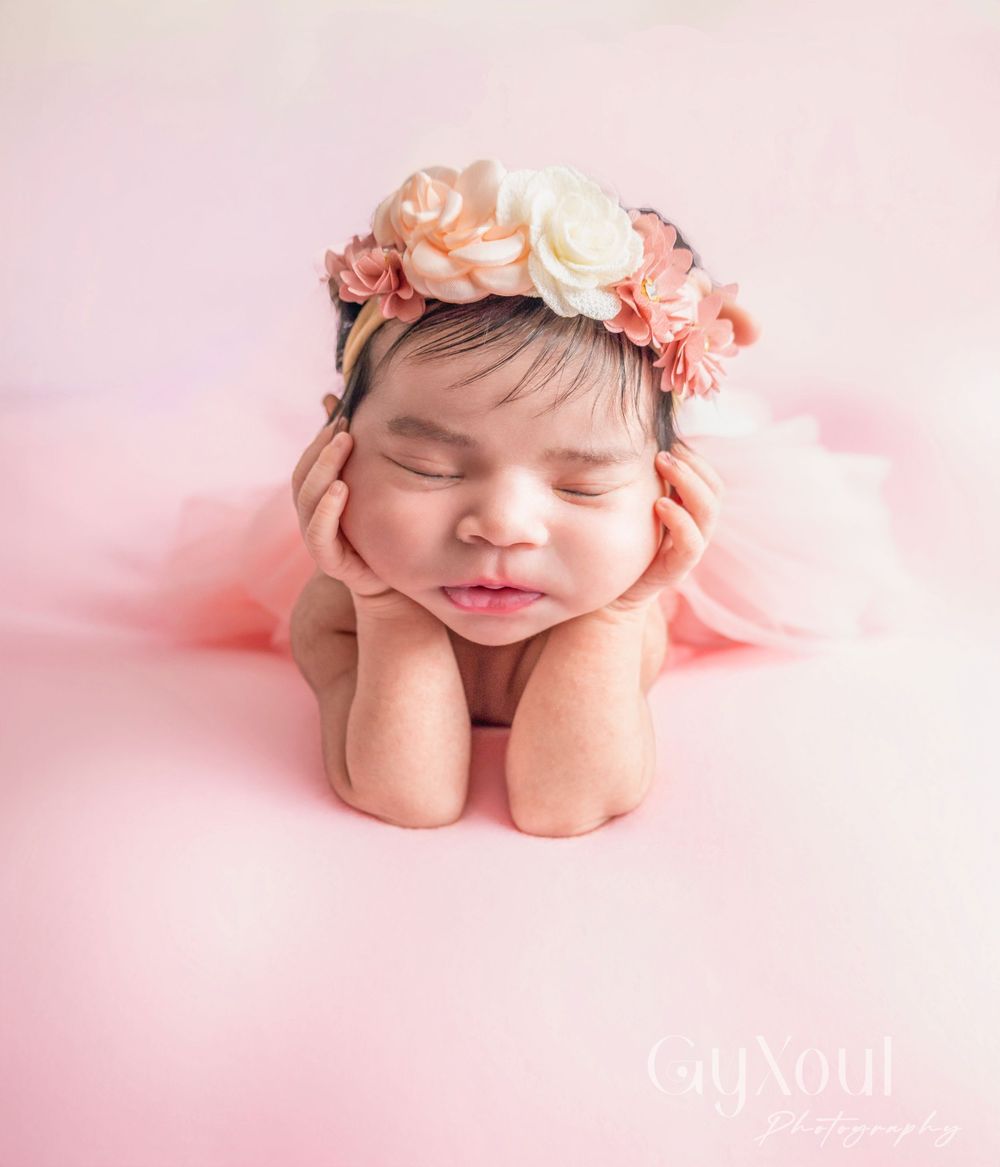 Sleeping newborn in pink floral crown resting on crossed arms.