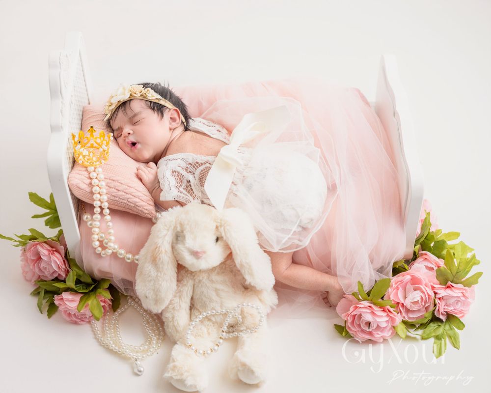 Sleeping newborn in tulle dress with bunny plush and floral decorations.