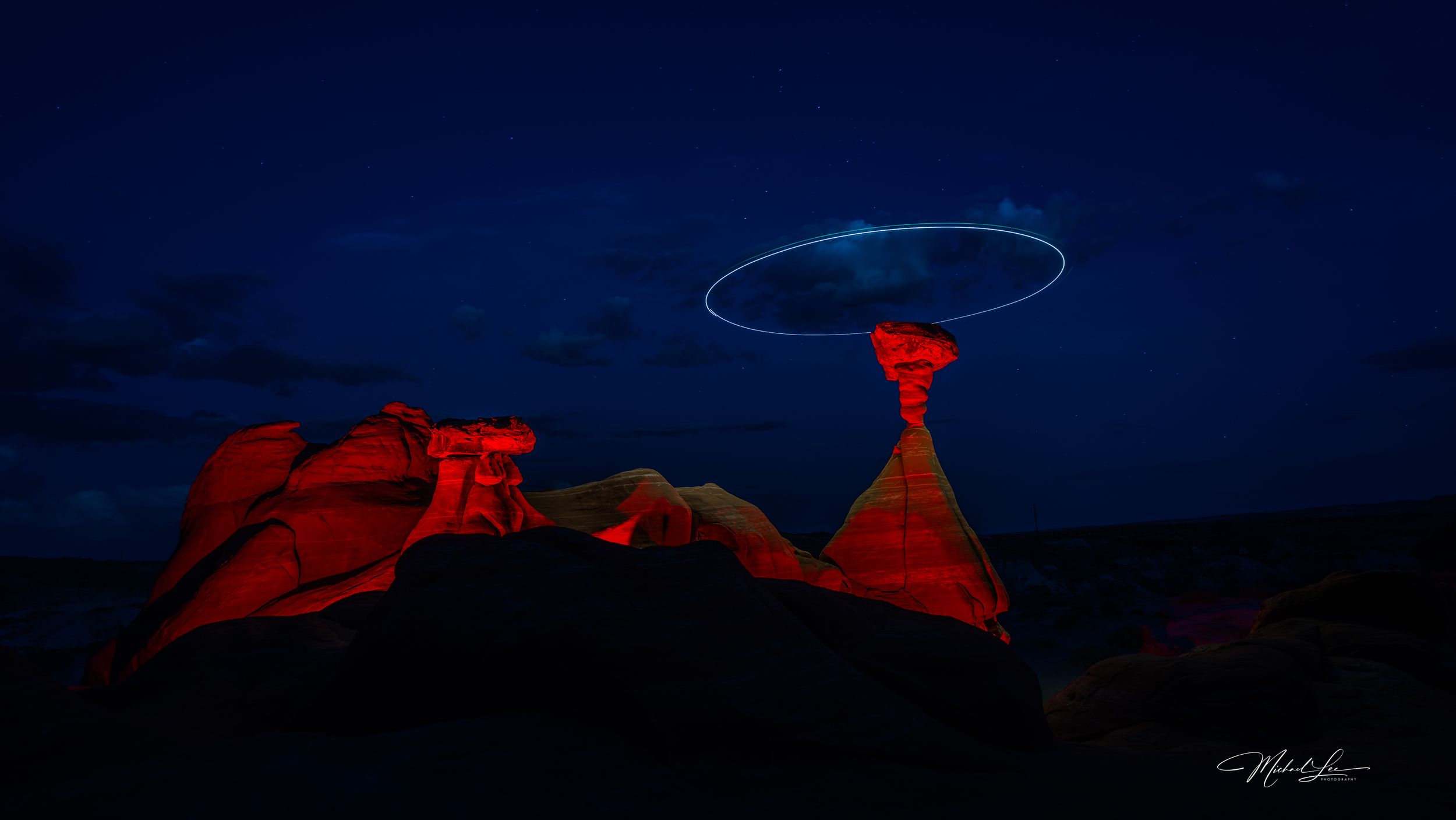 Light painting creates glowing halo effect over desert rock formations at night.