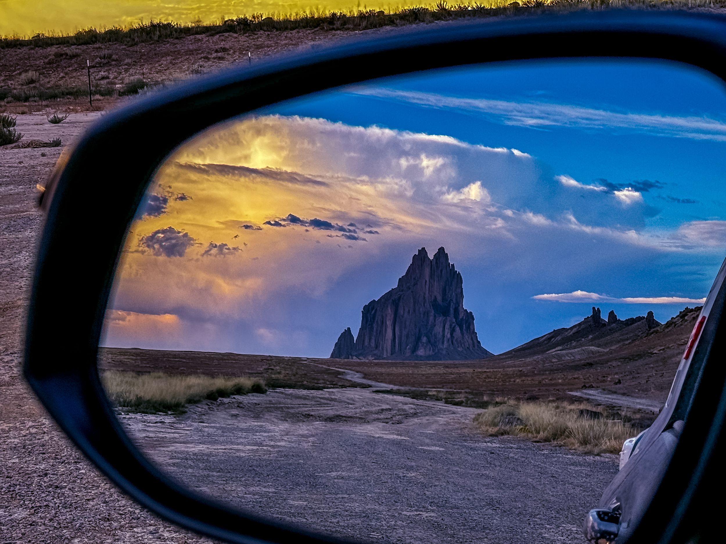 Shiprock peak formation reflected in car side mirror during sunset in New Mexico.