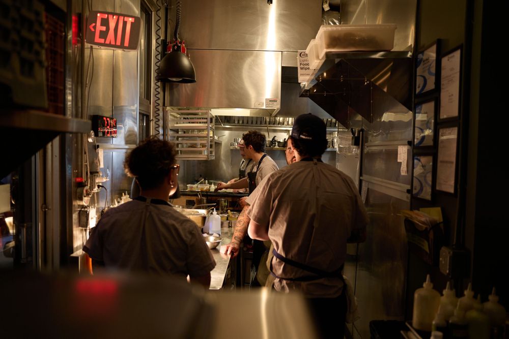 Restaurant kitchen staff working during evening service under red exit sign glow.
