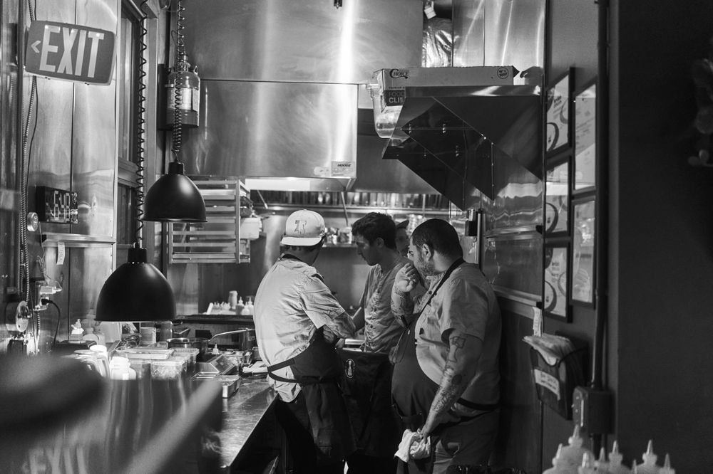 Kitchen staff working together in a dimly lit restaurant kitchen during evening service.