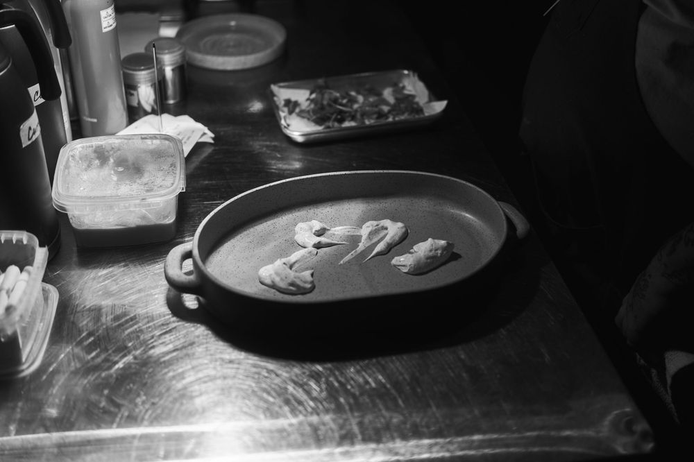 A rustic pan with ingredients sits on a stainless steel prep counter in low light.