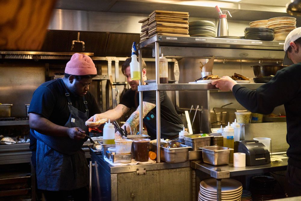 Restaurant kitchen staff preparing food under hanging industrial lamps during service.