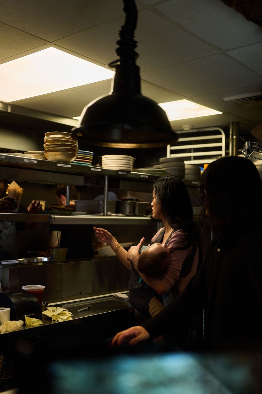 Restaurant kitchen staff member working under pendant lighting during service hours.