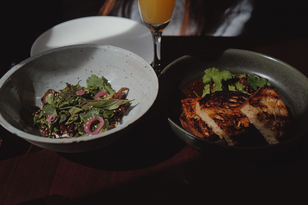 Restaurant plate presentation with salad and grilled meat dish alongside mimosa.