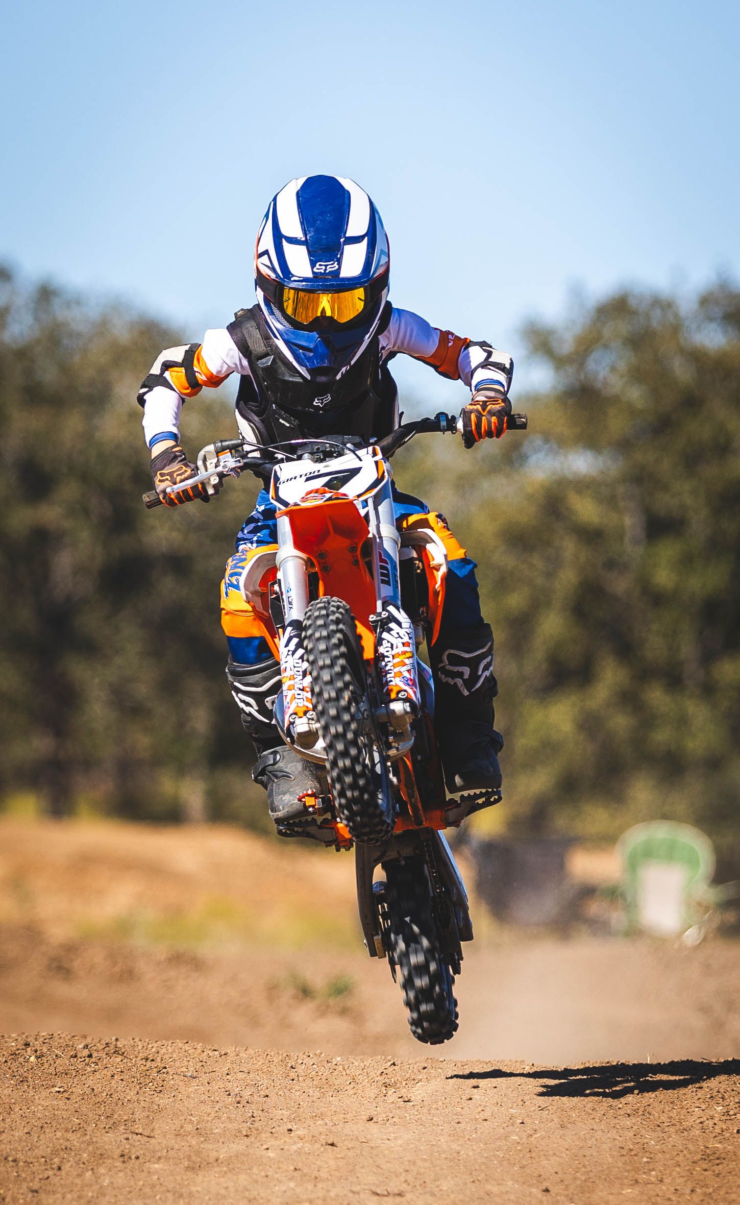 Dirt bike rider performing airborne jump on a motocross track with protective gear and blue helmet.