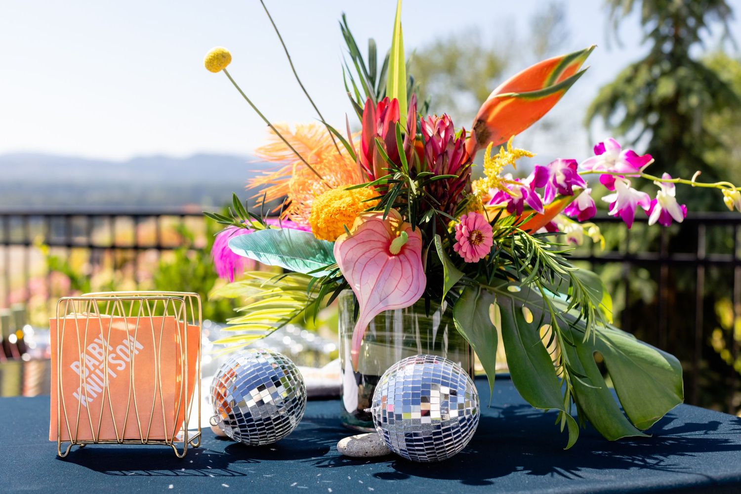 Vibrant tropical floral centerpiece with pink and orange blooms beside silver mercury glass votives and coral decor.
