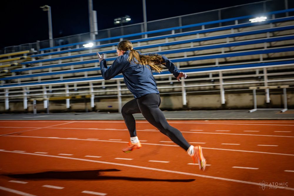 Action shot of a female sprinter racing down the track under the lights at night.