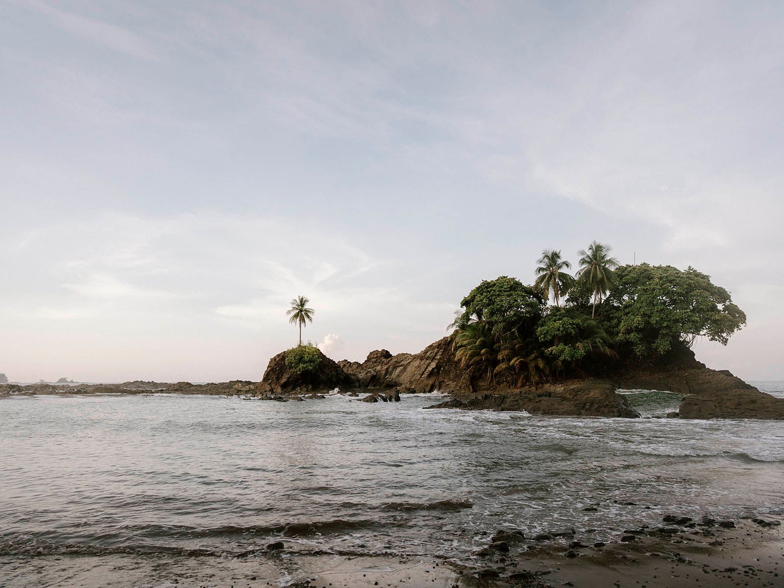 Panoramic view of a tropical island with palm trees and rocky coastline during sunset.