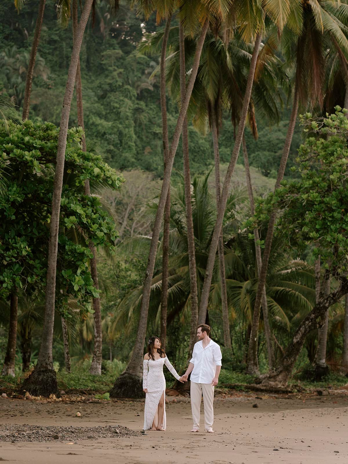 Palm tree lined beach path with two people in white clothing walking together.