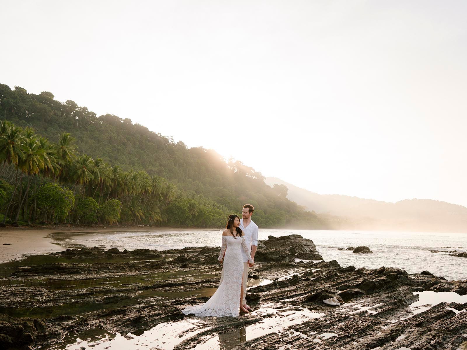 Romantic beach photoshoot on rocky coastline during golden hour.