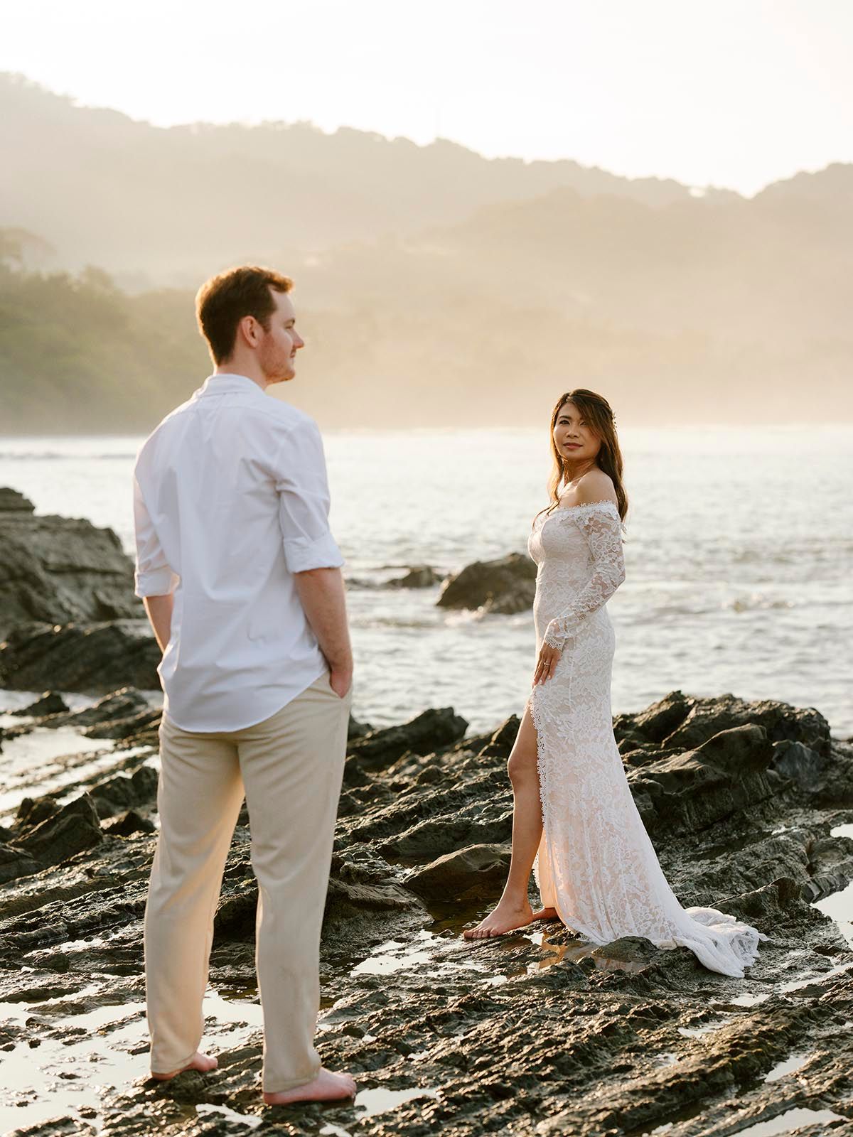 Couple exploring rocky beach coastline during sunset in tropical setting.