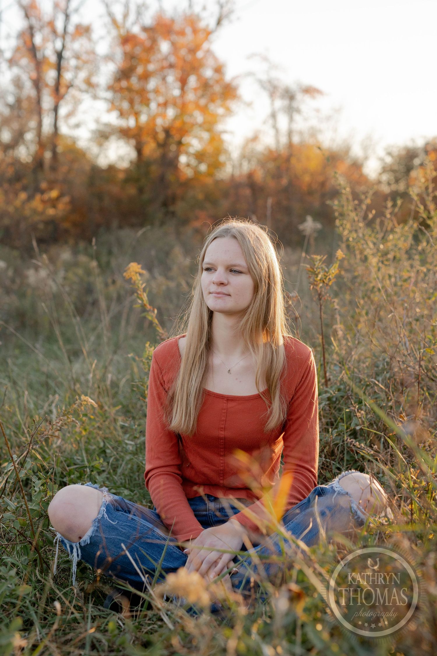 Person in coral sweater sits peacefully in autumn field during golden hour.
