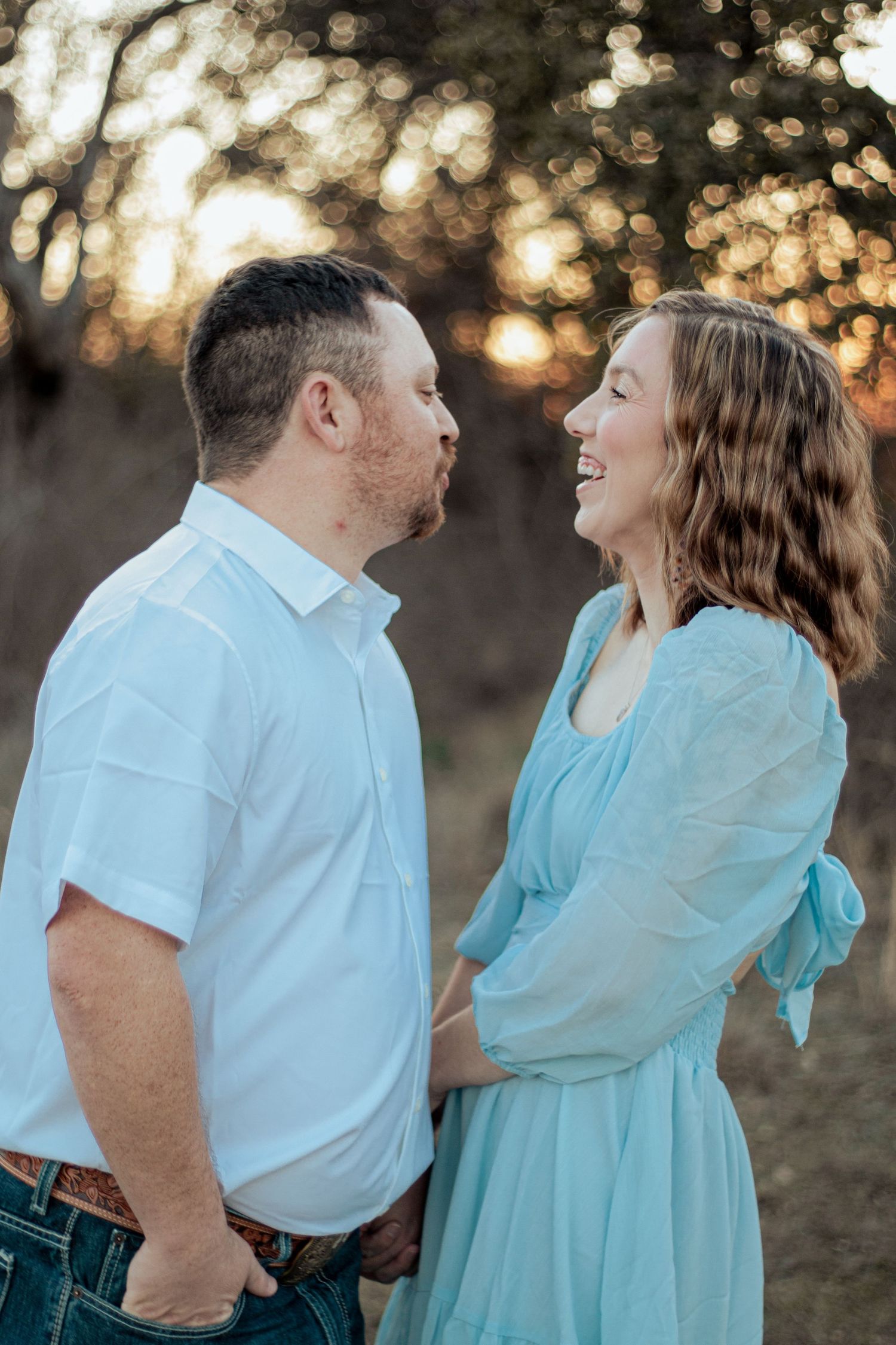 A couple shares a joyful moment at sunset, with warm bokeh lighting in the background creating a romantic atmosphere.