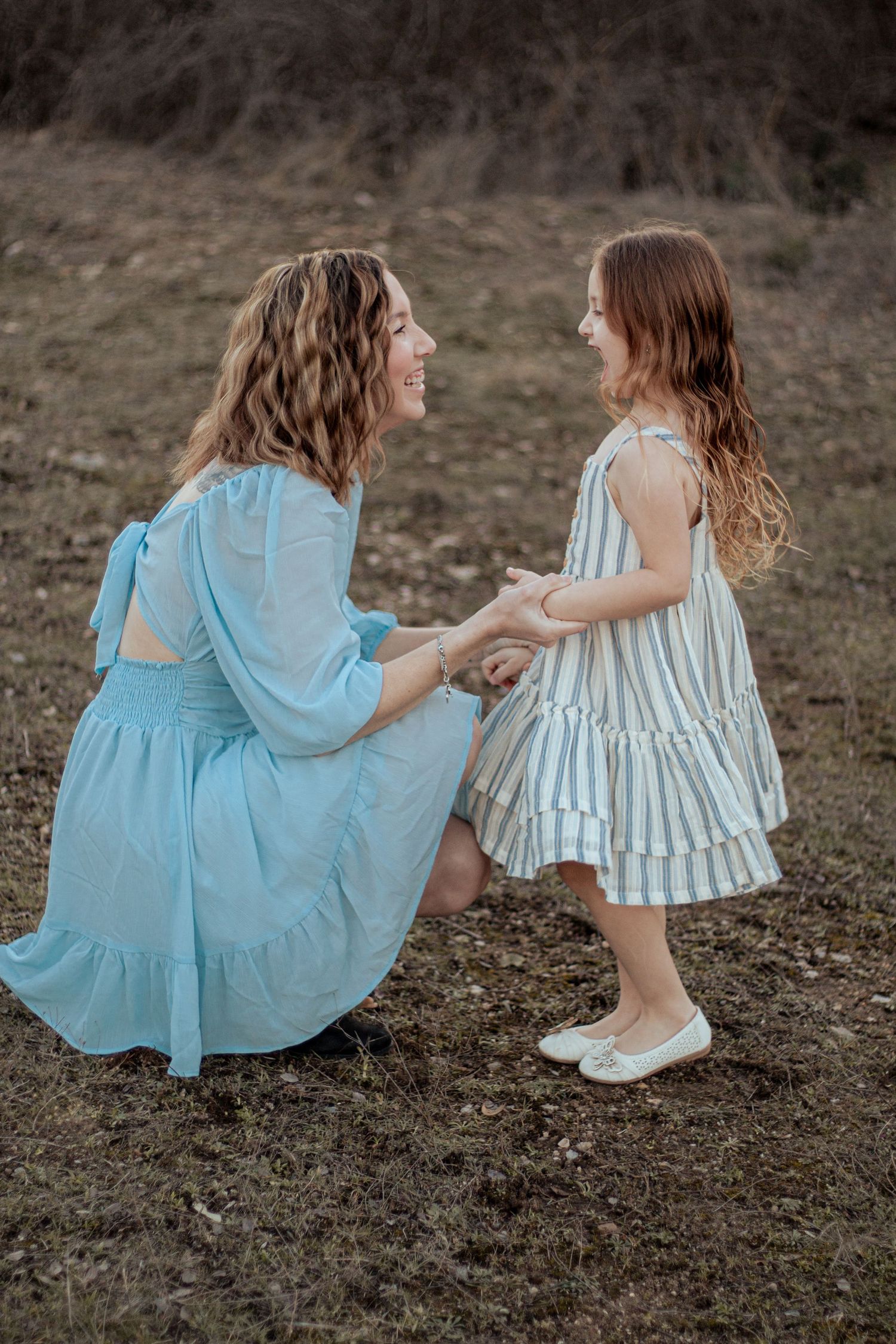 Two people in matching blue and white dresses hold hands while sharing a tender outdoor moment in a field.