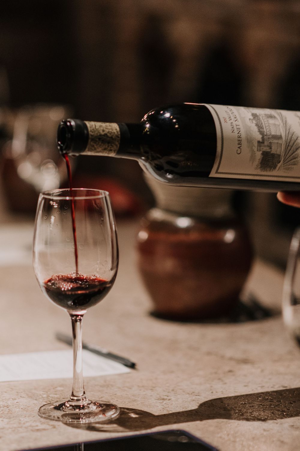 An artistic photo of a wine glass with red wine being poured into it.