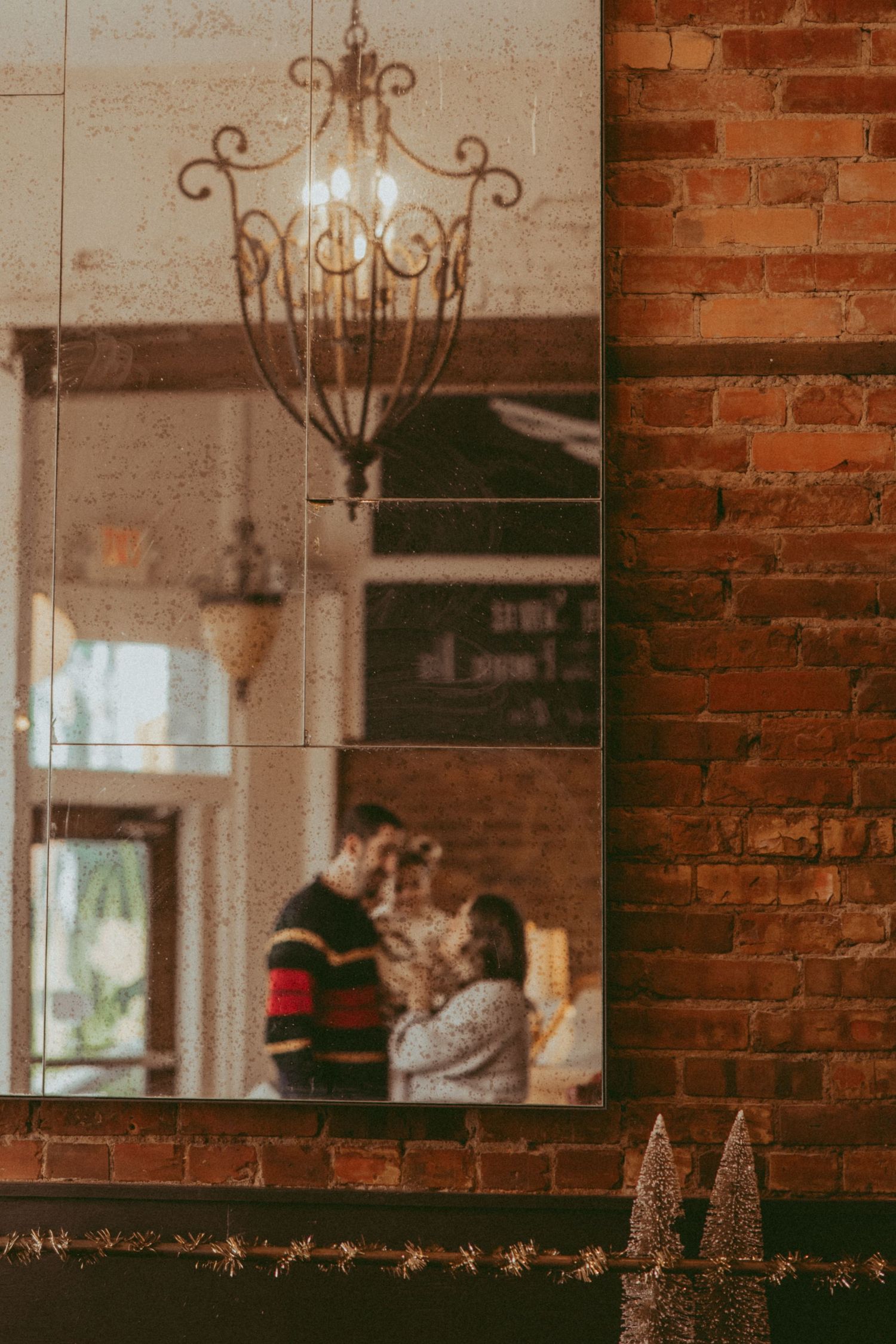 Rustic brick wall interior with elegant hanging chandeliers and mirrors creates warm, vintage ambiance.