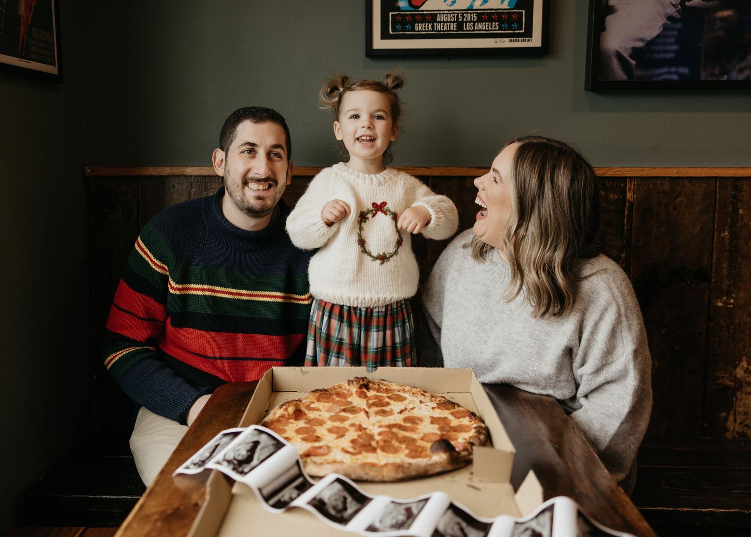 Family sits at a wooden table with pizza and drinks while looking at an ultrasound photo together.