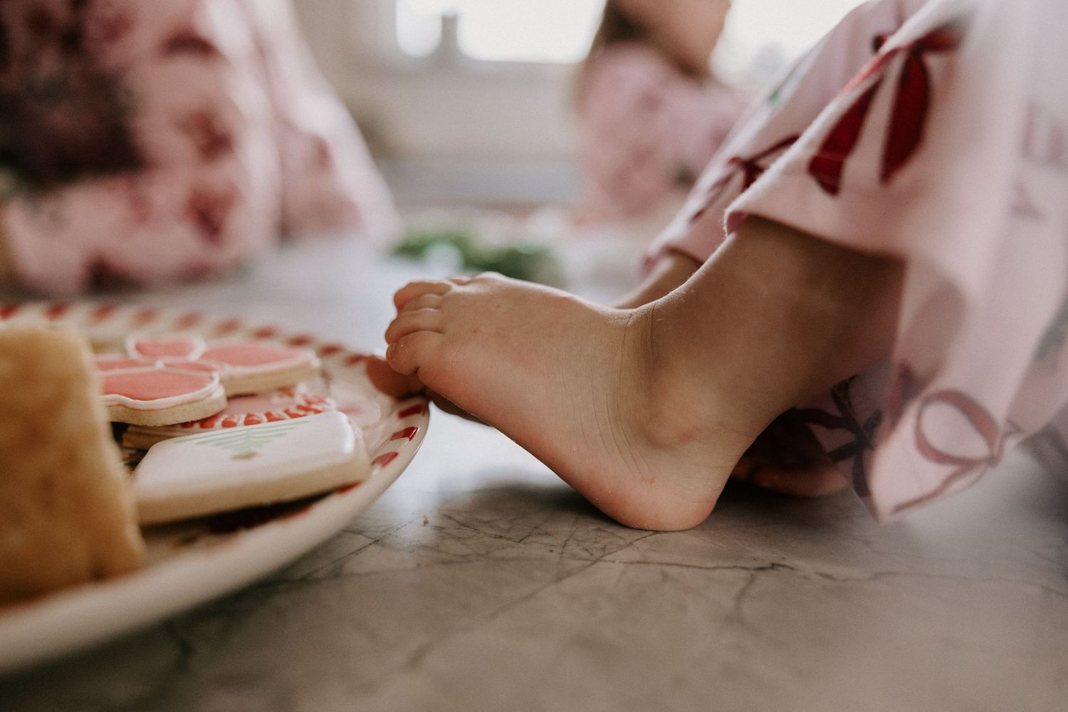 A person slices into a pink frosted sugar cookie with a knife on a white plate.