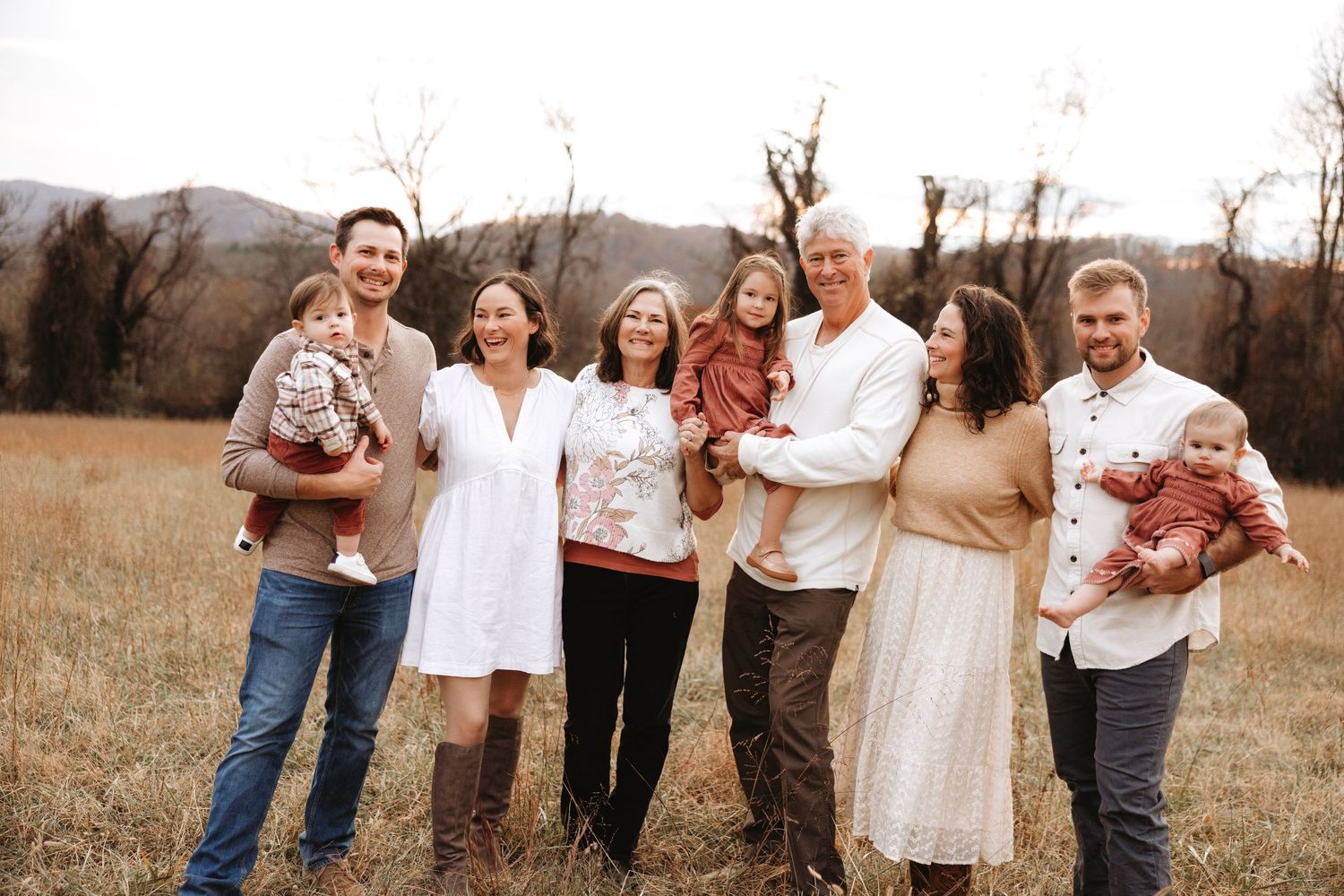 A group stands together in a brown autumn field at sunset wearing coordinated neutral-toned outfits.