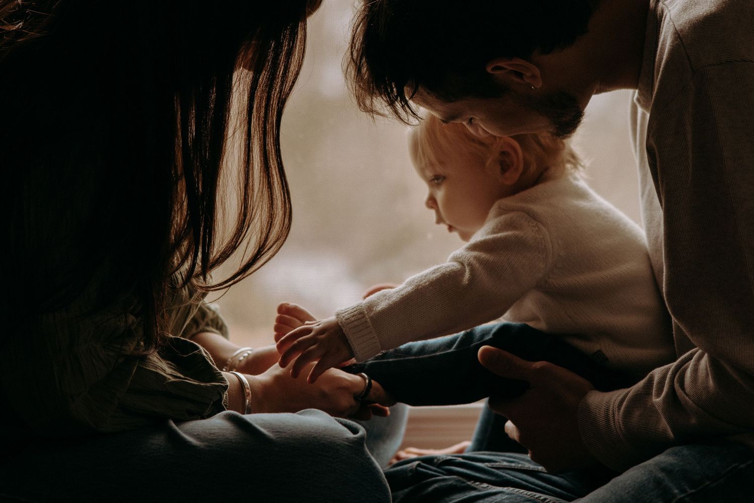 A series of intimate black and white photographs showing tender moments between parent and child in window light.