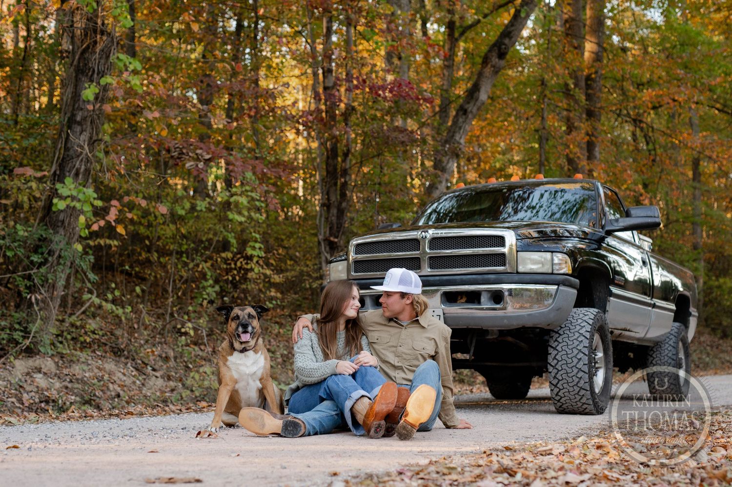 People and their dog relax on a forest path beside a lifted black pickup truck.