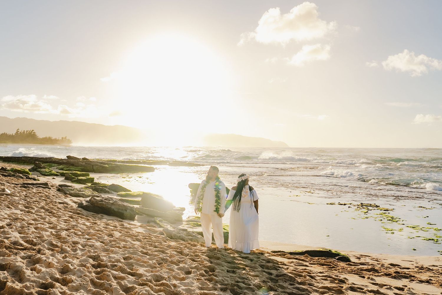 Wedding guests toss pink flower petals on a scenic beach while celebrating with joyful expressions and colorful attire.